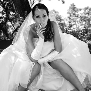 Esküvői jegyesfotózás menyasszony dohányzik padon ülve vicces